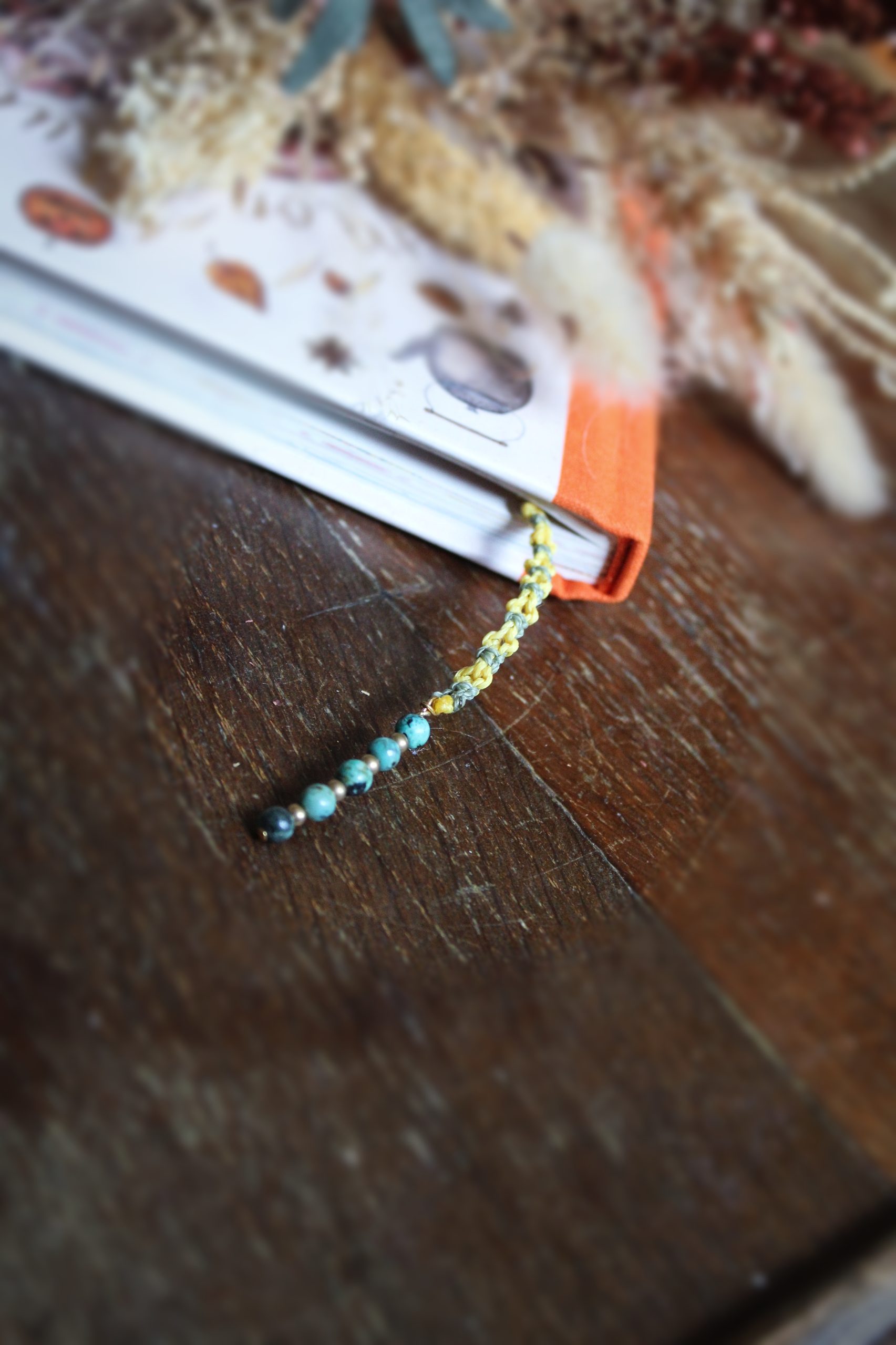 Marque page jaune et vert avec des perles de turquoise africaine en micro macramé dans un livre